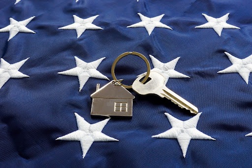 A keychain with a silver house and key laying on top of the stars of the American flag.