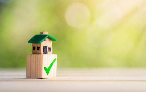 A small wooden house on top of a wooden block with a checkmark on it