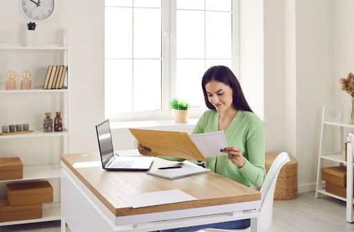 Alt: A woman sitting at a table reviewing an envelope of documents.