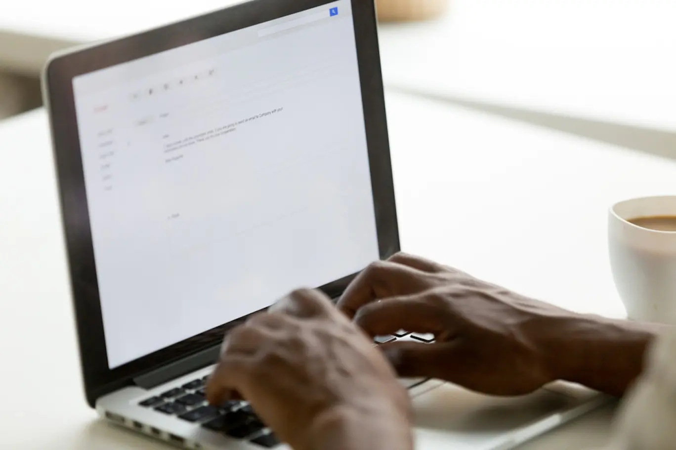 Close up of a Black person’s hands typing a letter on their laptop.