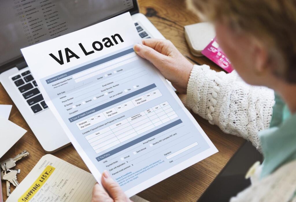 Woman holding a VA loan application while sitting at a desk cluttered with papers and her laptop.