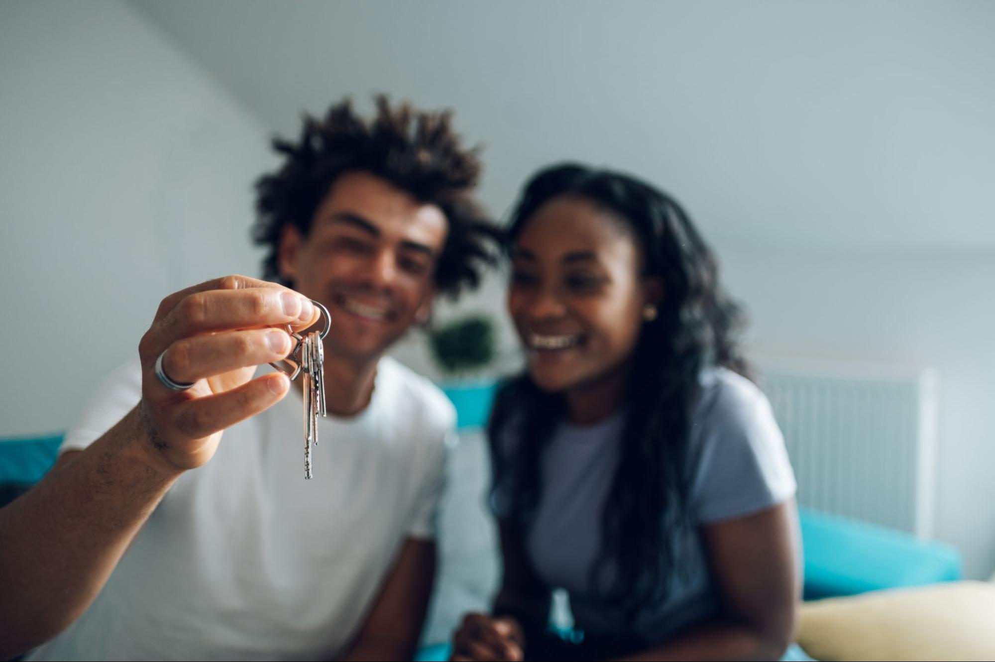 A couple holding a set of keys in focus.