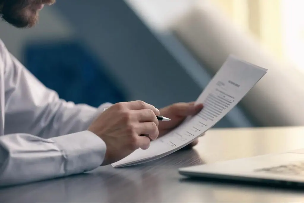 Close up of a businessman in a button-up sitting at a desk holding a pen and reading a letter.