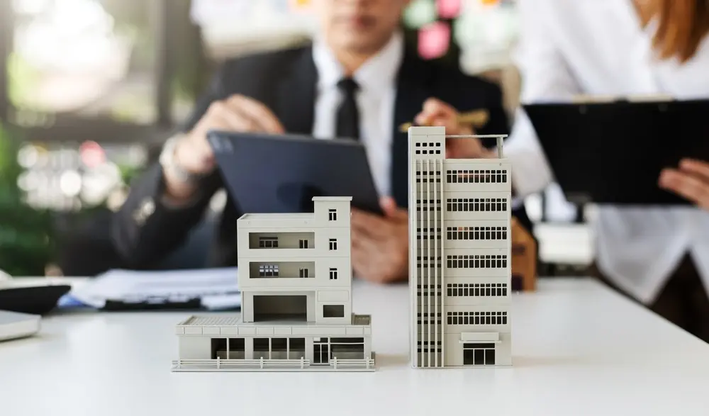 A man and woman speaking while looking at tablets and two real estate mockups in the forefront of the image.