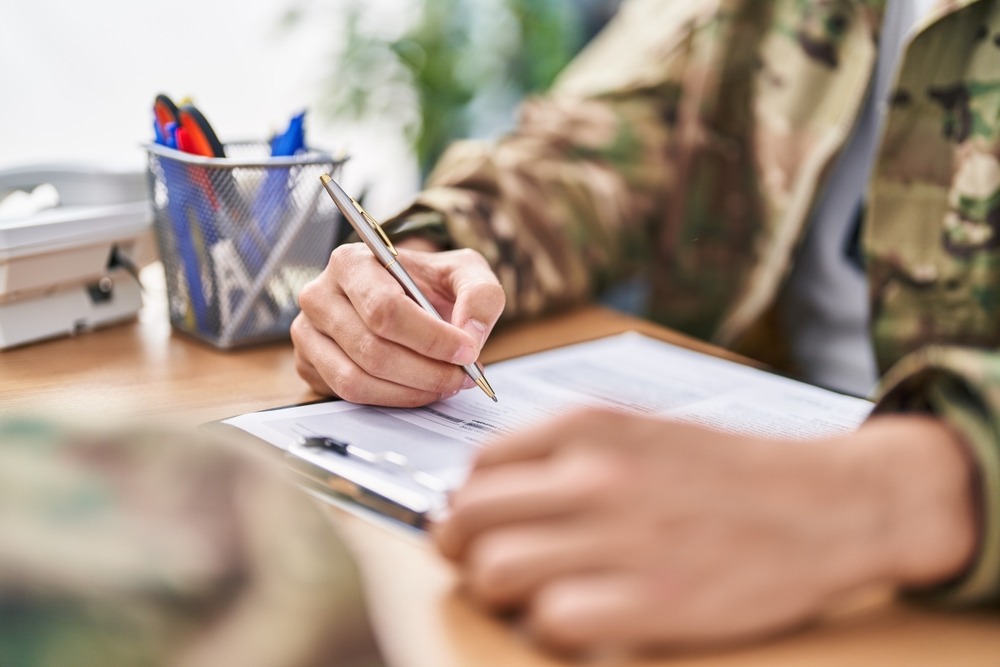 Man in military uniform sitting at a desk filling out paperwork.