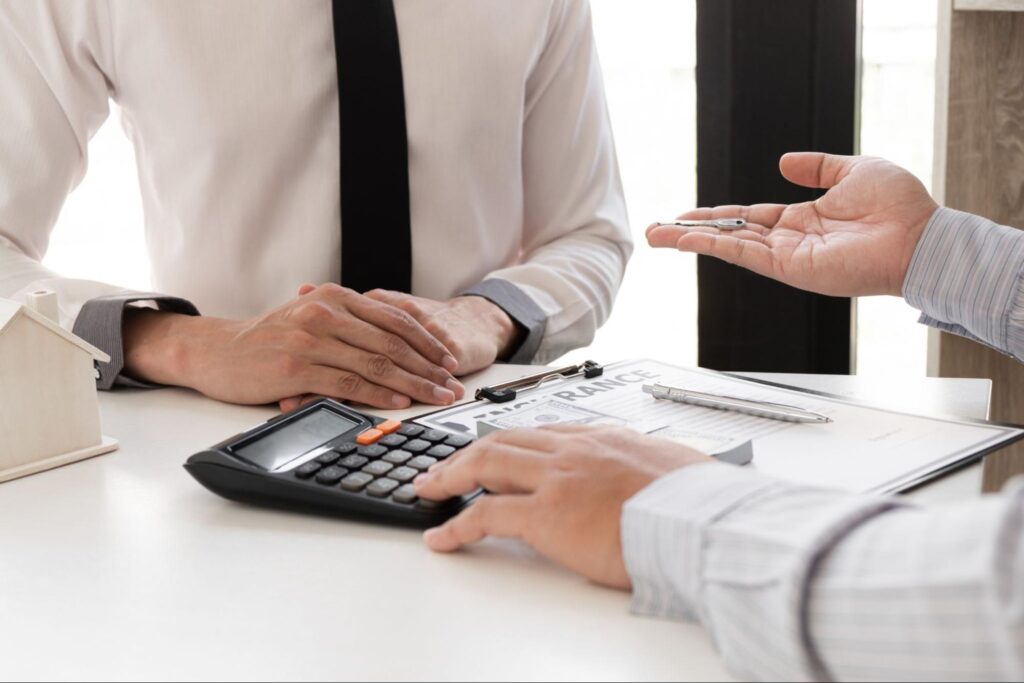Image of two men speaking at a table, one has his hand on a calculator explaining something.