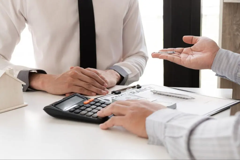 Image of two men speaking at a table, one has his hand on a calculator explaining something.