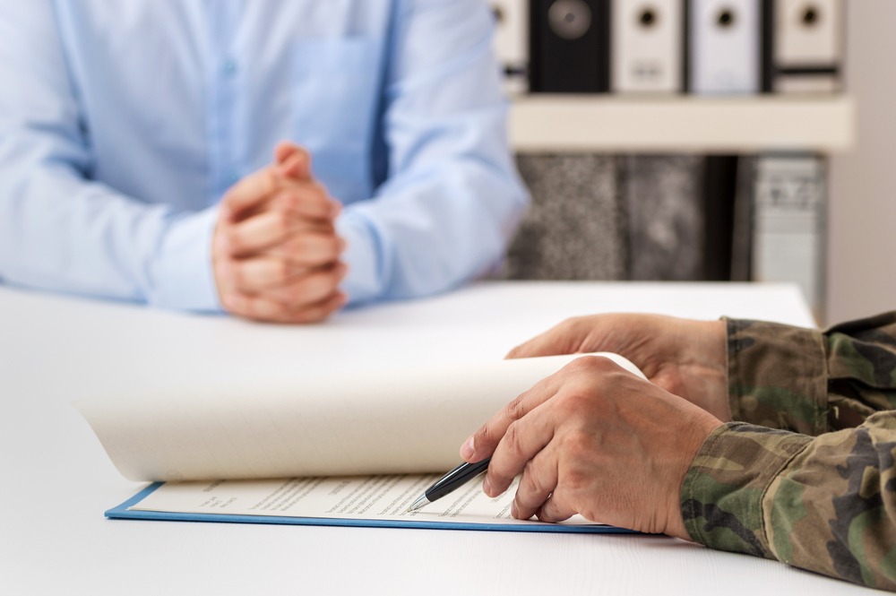 Close up of person’s hands signing paperwork while wearing a military uniform.