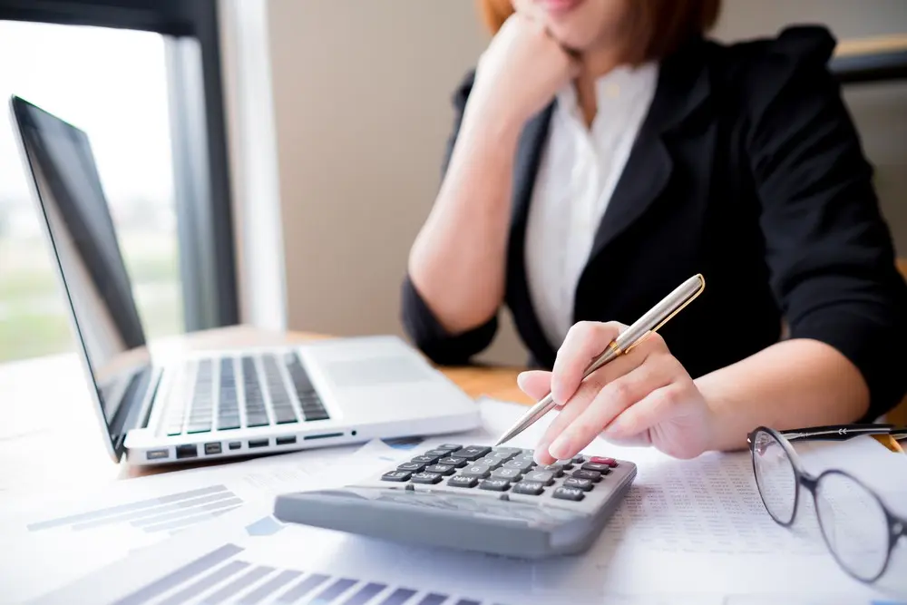 Woman sitting at desk using a calculator and laptop.