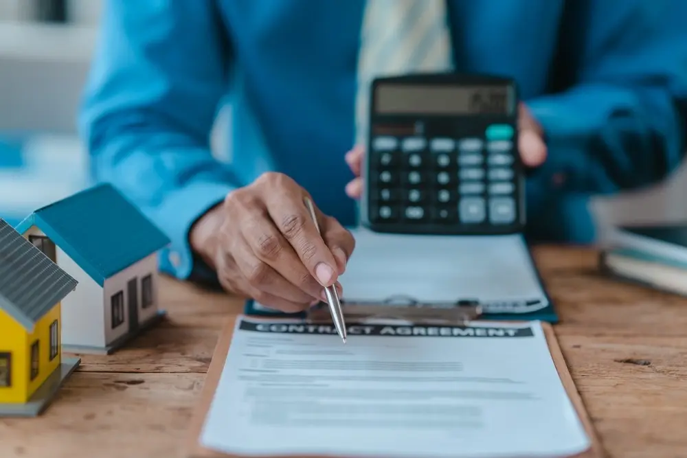 Loan officer sitting at a desk with a loan agreement in front of him. He is showing a calculator to the viewer.