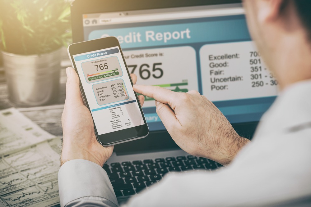 Image of man sitting in front of a laptop checking his credit score of 765 on his phone.