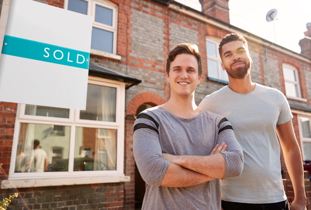 Two men standing outside of a home with a sold sign.