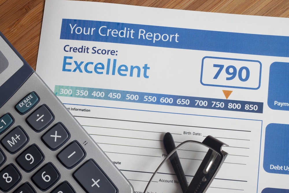 A credit report with an excellent score of 790 lies on a table with a calculator and a pair of eyeglasses on top of it.