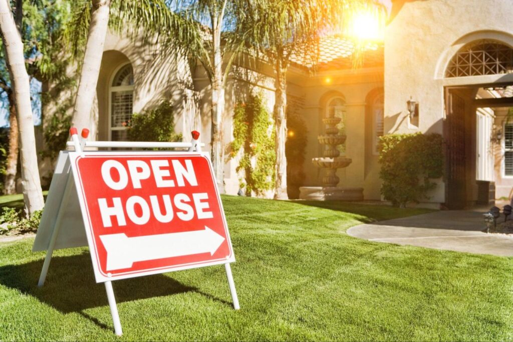 The sun shining on a red and white open house sign propped up on a grassy front lawn.