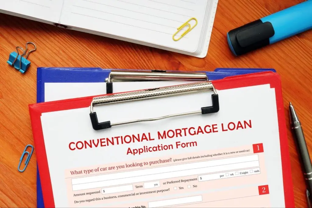 A red clipboard stacked on top of a blue clipboard has a conventional mortgage loan application form attached to it.