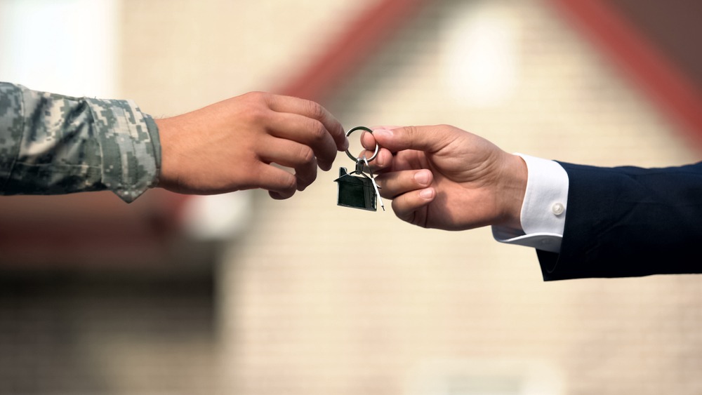 Man in a business suit giving house key to military service member.