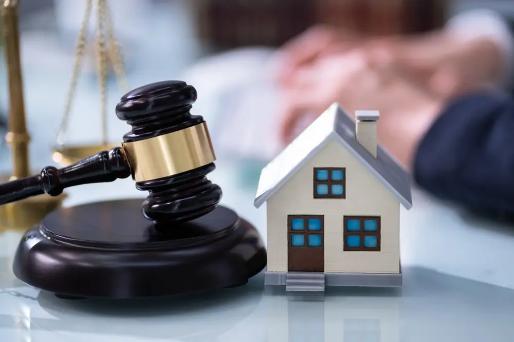 A gavel sits next to a small model of a home.
