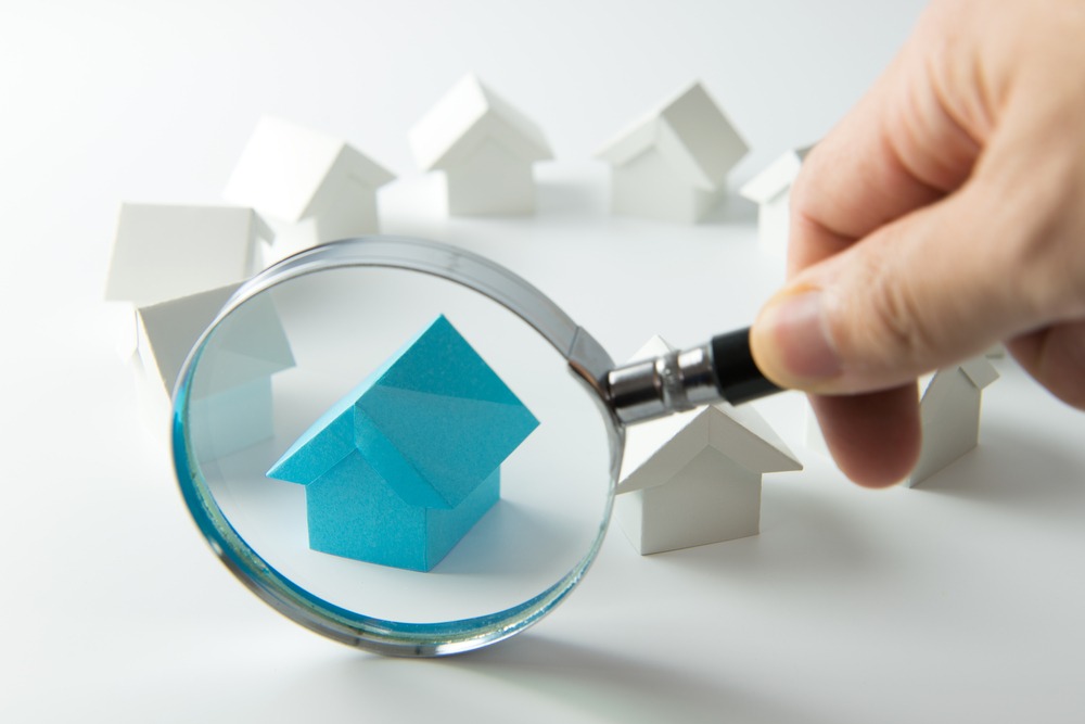 A magnifying glass is held over a blue home model that’s surrounded by other white home models.