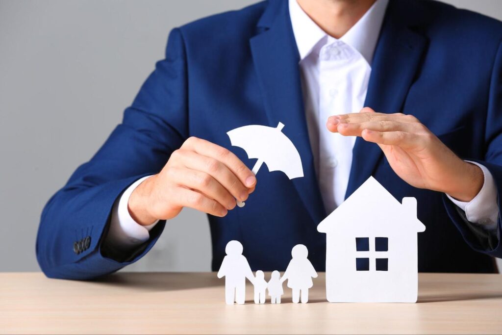 Man covering paper family and home with a paper umbrella cutout.