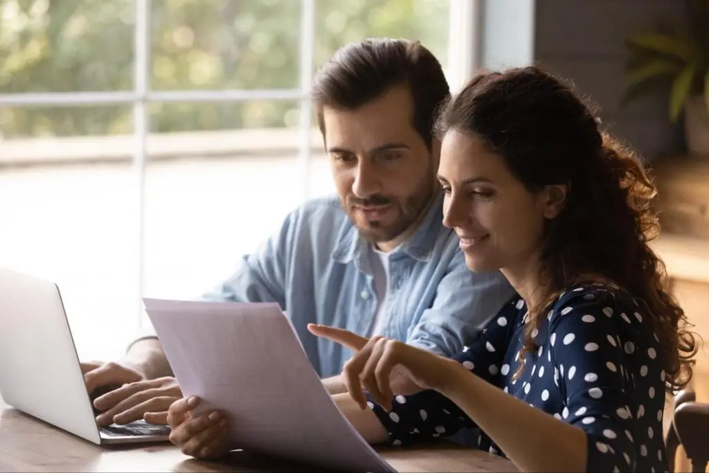 A man and woman sit at a table with an open laptop and review their mortgage statement.