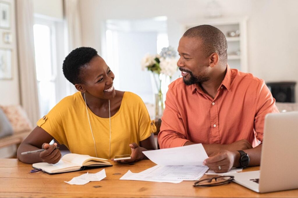 Smiling African-American Couple Talking About Refinancing Adjustable-Rate Mortgage.