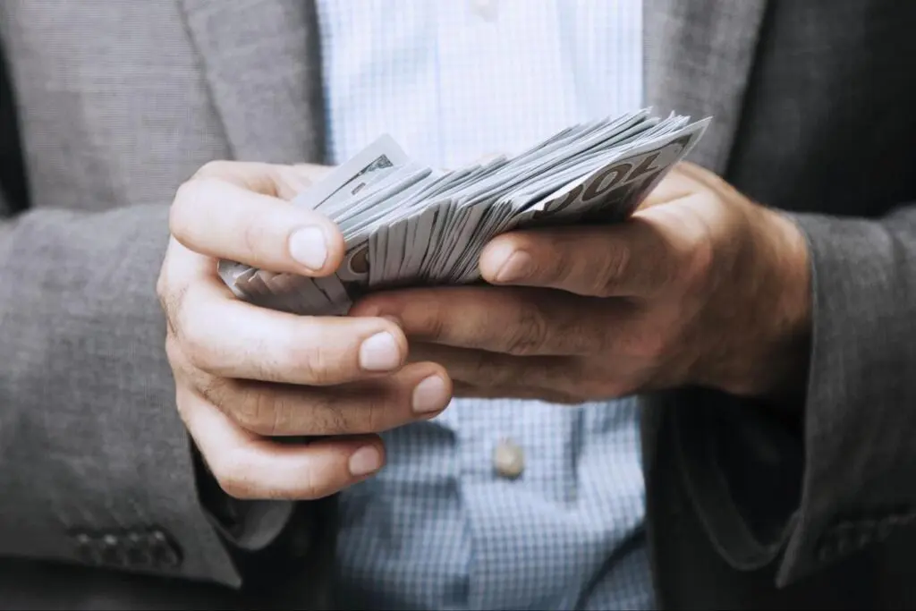 Man holding several hundred dollar bills in hand.