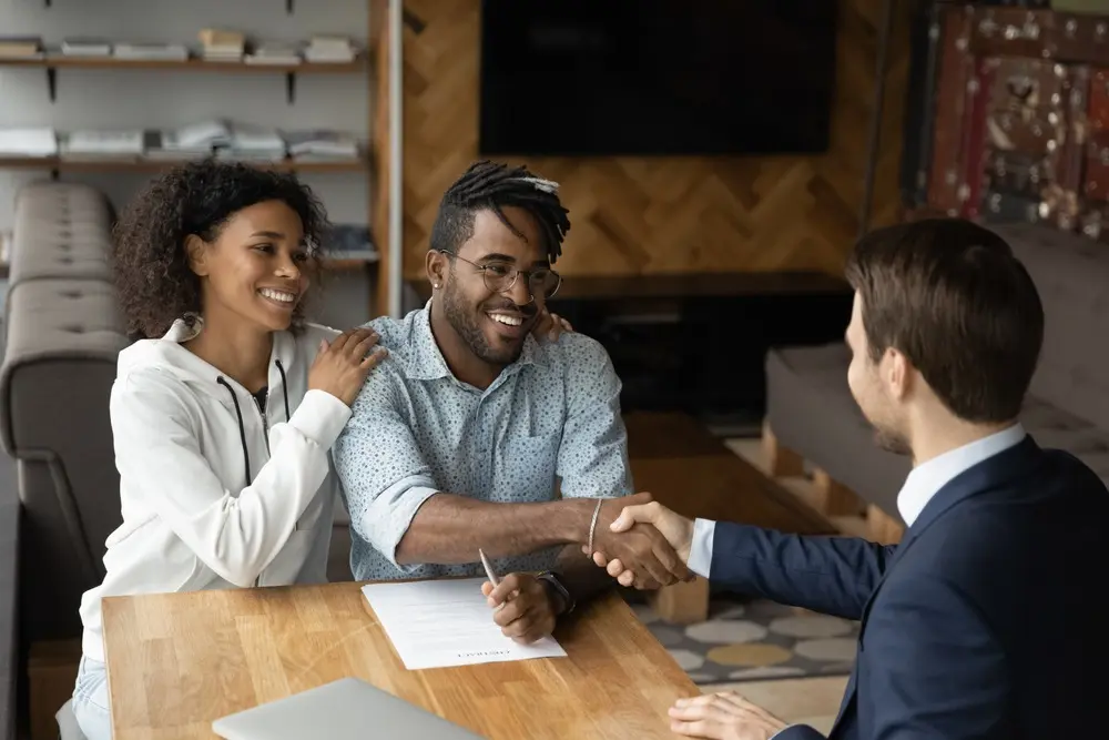 Couple signing a contract and shaking hands with a lender in an office.