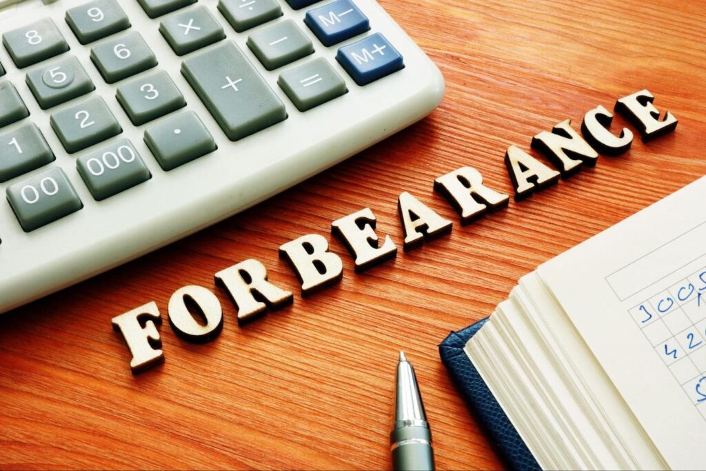 “FORBEARANCE” is spelled out on a table between a calculator and a ledger.