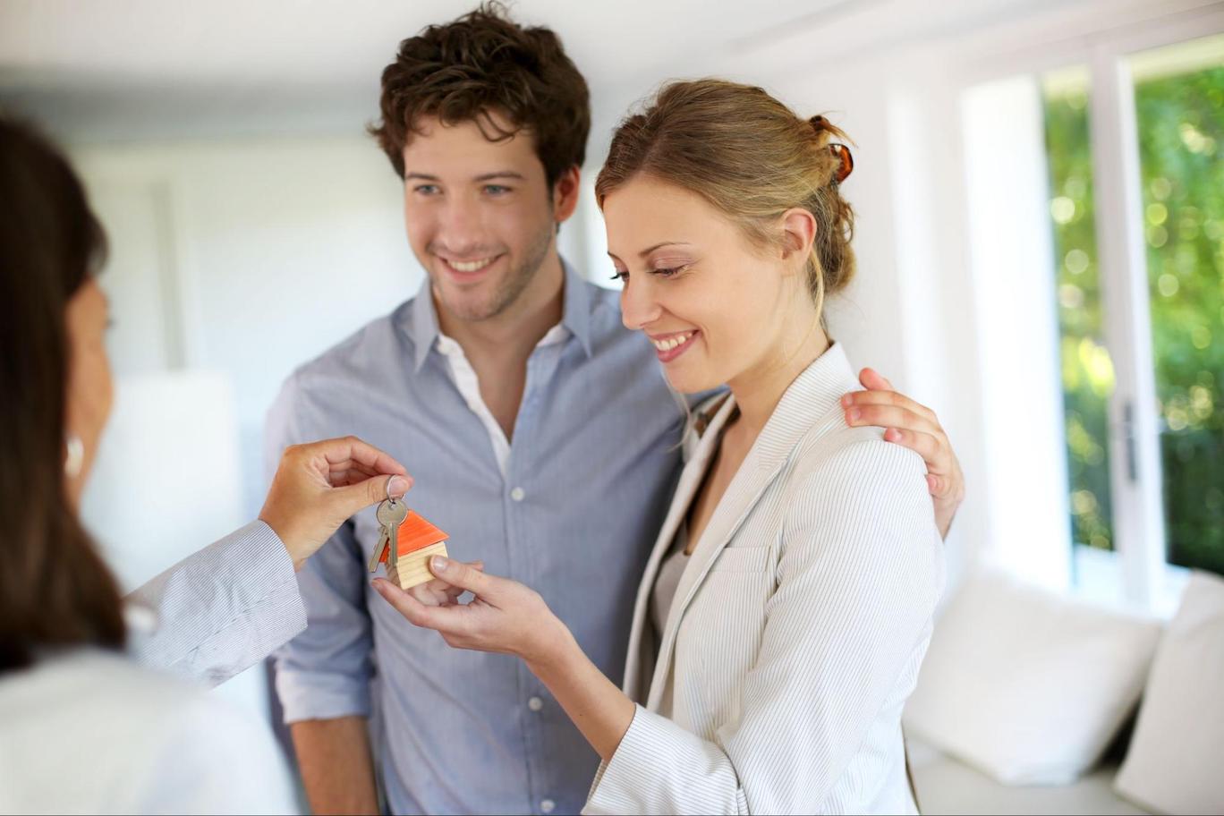 A woman hands new house keys over to a smiling white couple.