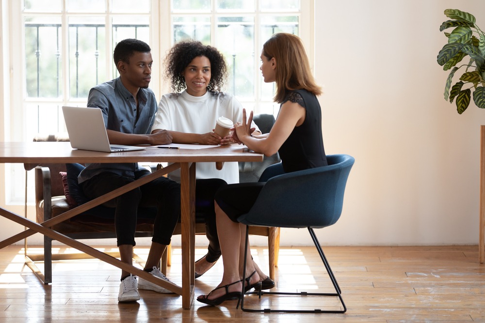 A young black couple sits at a table and speaks with their mortgage lender. 