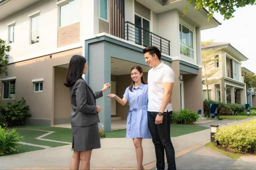 A real estate agent hands a young Asian couple the keys to their new home.