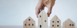A hand lifting up a wooden model home situated alongside a series of other wooden model homes.