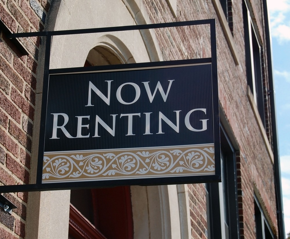 A sign that reads “NOW RENTING” protrudes from the side of a brick building.