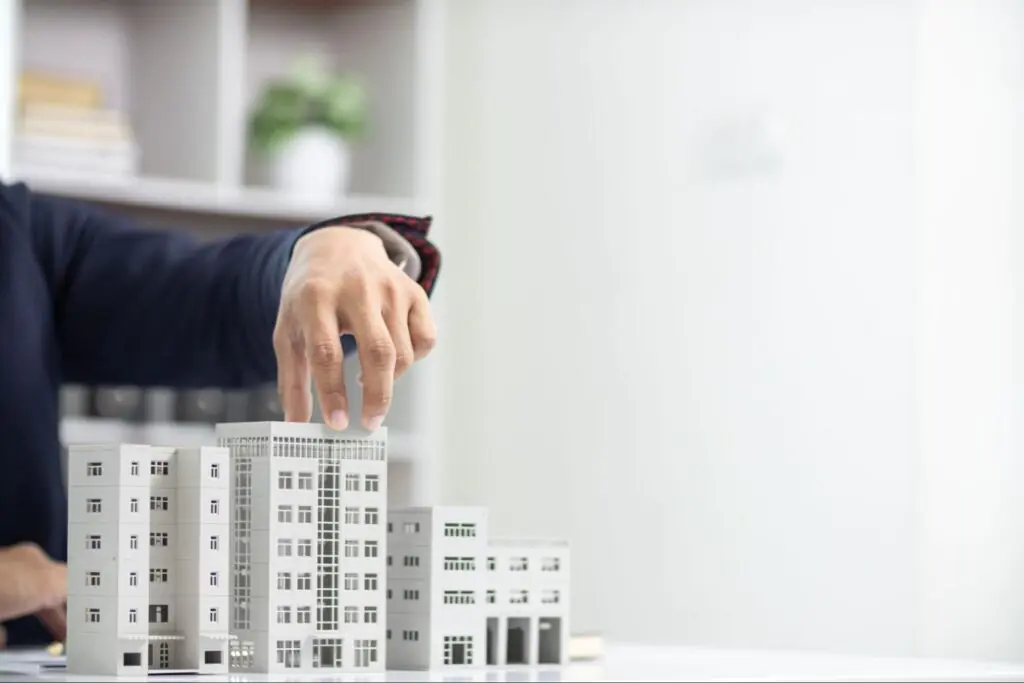 A person in a white office touches the top of a model of a real estate development.