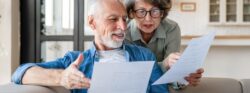 An elderly white couple review documents on their couch.