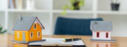 An orange and a white model home sit on a wooden desk alongside a contract on a clipboard.