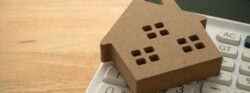 A brown model home sits on top of a handheld calculator.