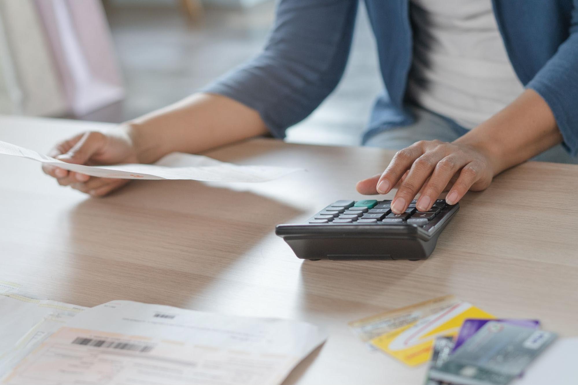A person types on a calculator while looking at a document with the other hand.