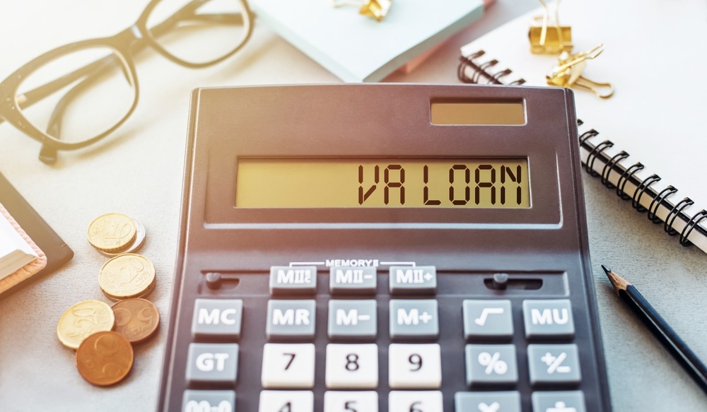 A handheld calculator spelling out “VA LOAN” sits on a cluttered desk. 