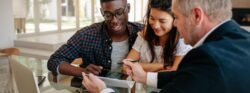 A mortgage lender shows an excited young couple a document.