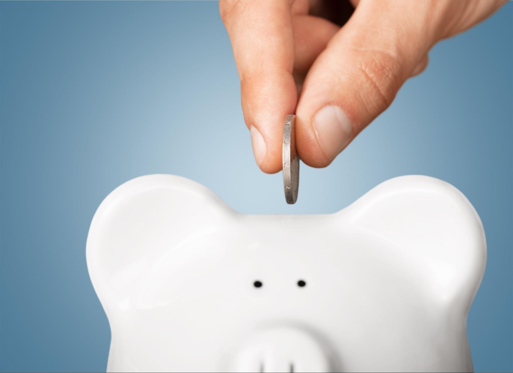 A person inserting a coin into a white piggy bank.