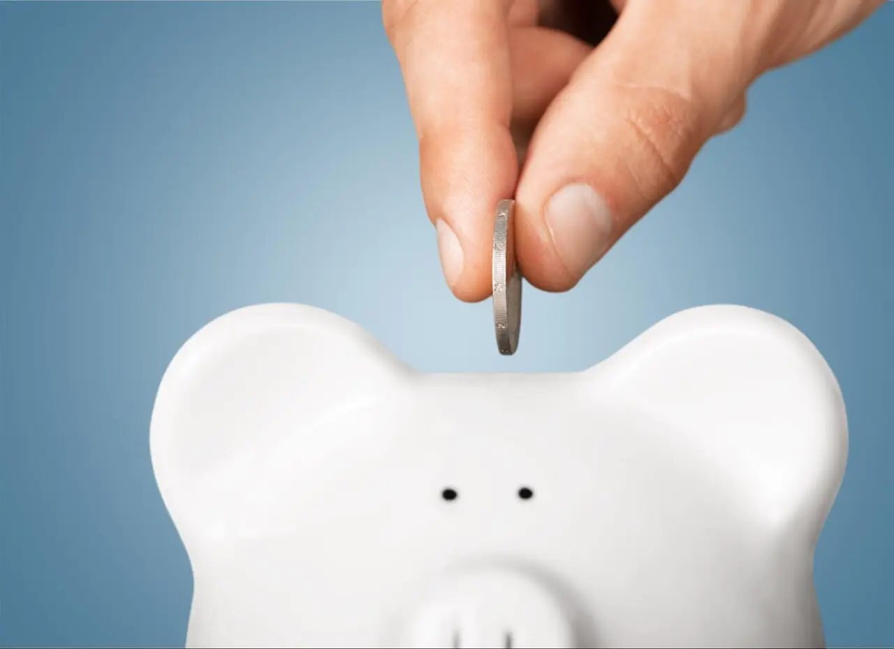 A person inserting a coin into a white piggy bank.