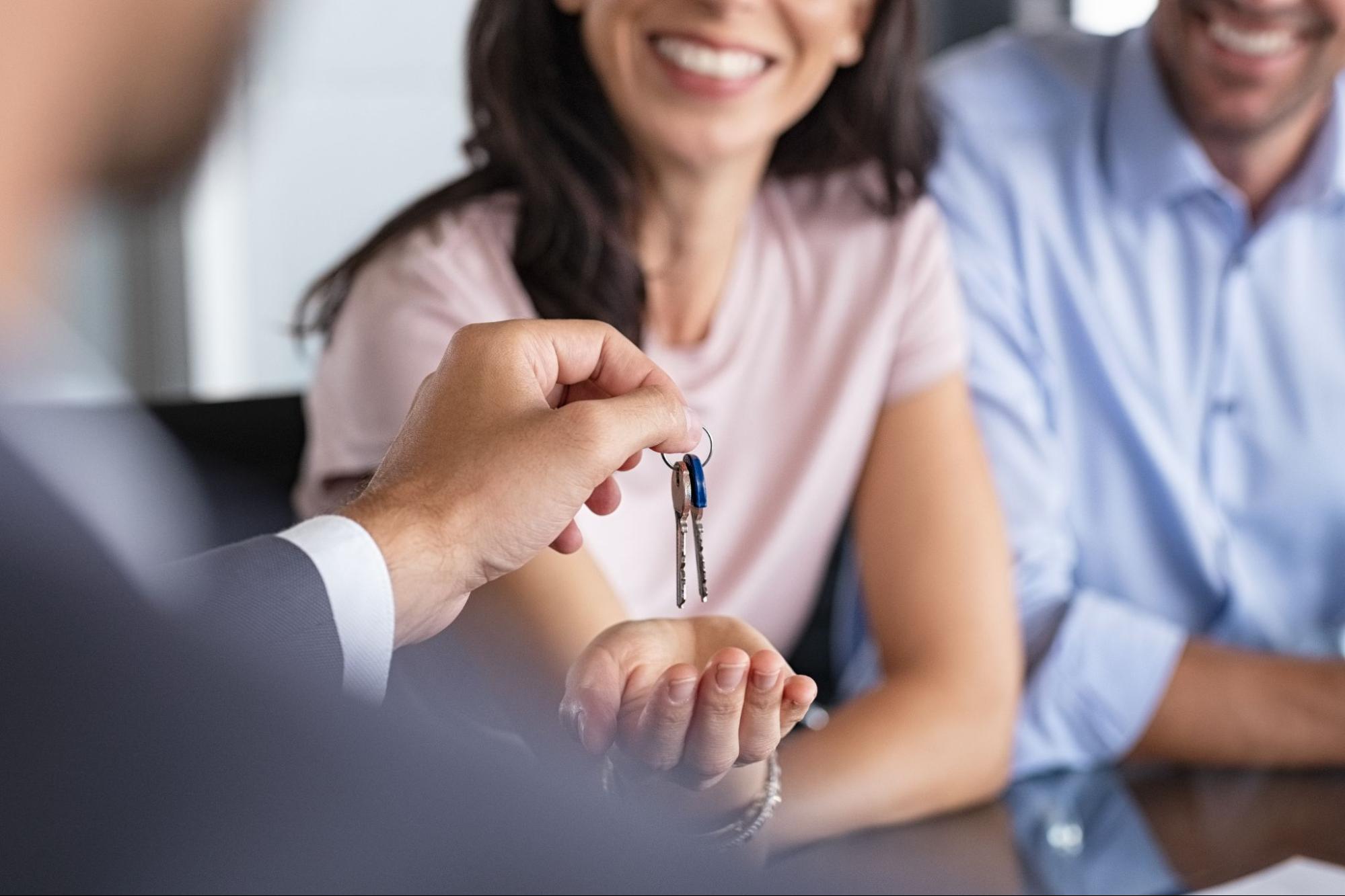 A mortgage lender handing the keys to the home to a smiling couple.