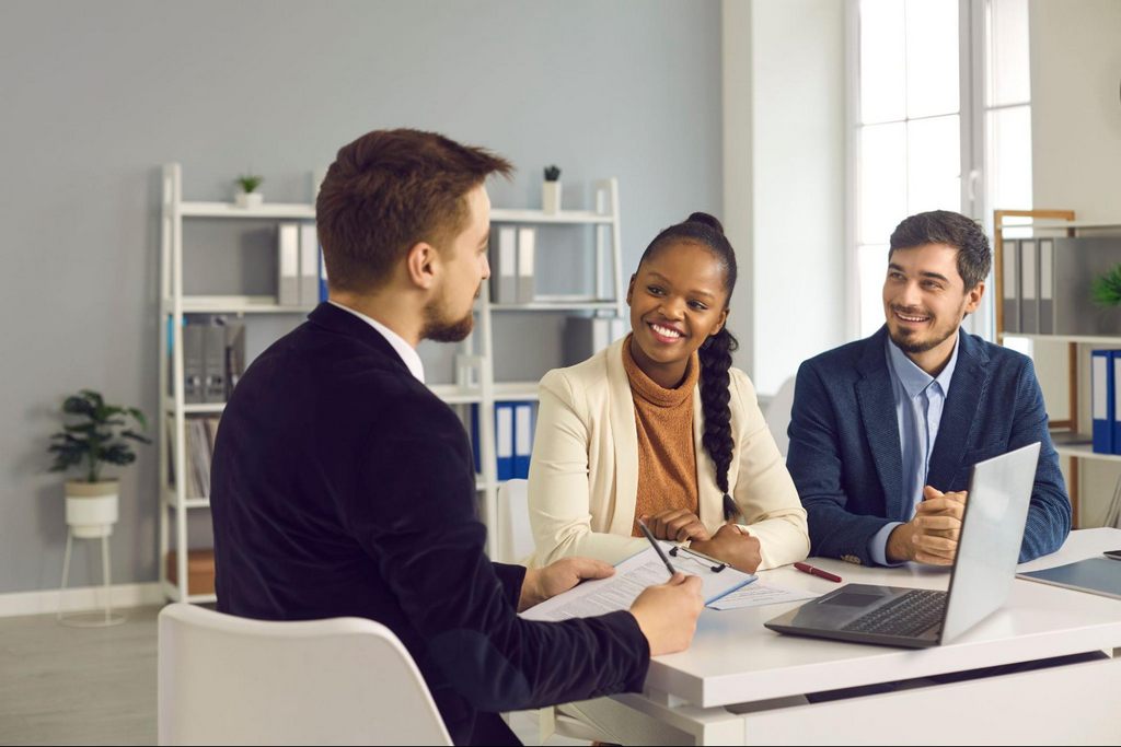 A young smiling couple sitting in an office speaking with their mortgage lender. 