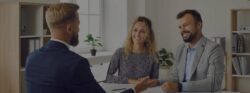 A young white couple sitting in a bright office and speaking with their mortgage lender.