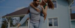 A man giving his wife a piggyback ride in front of the home they just purchased.