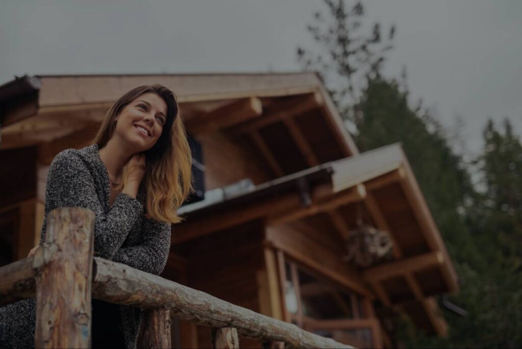 A smiling white woman leans on the balcony of her vacation home.