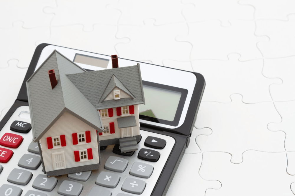 A model home sitting on a calculator and puzzle.