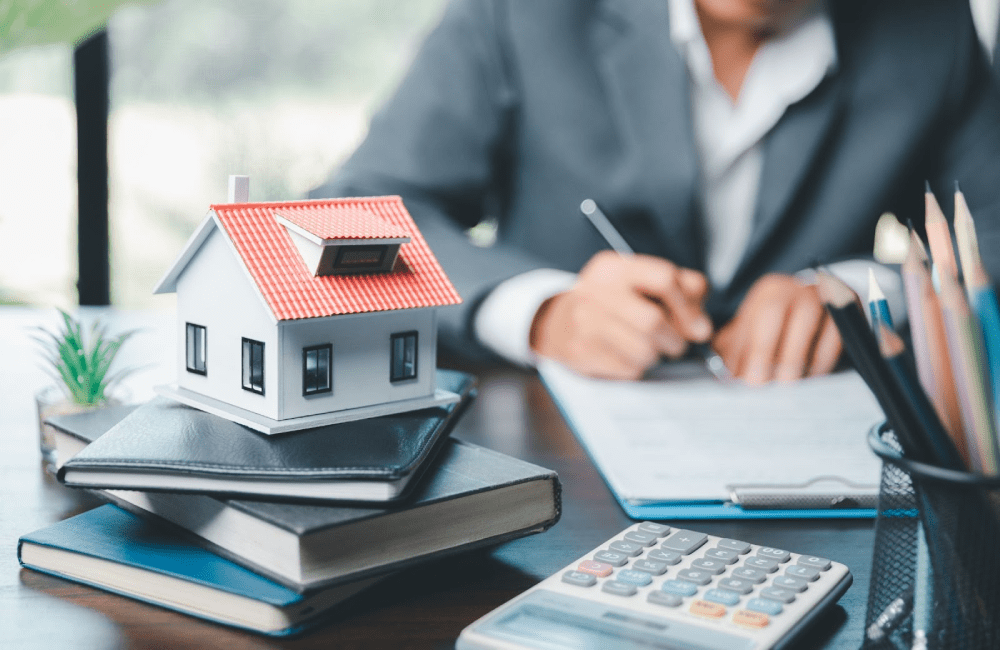 A model home sitting on a stack of notebooks next to a calculator in the office of a mortgage lender.