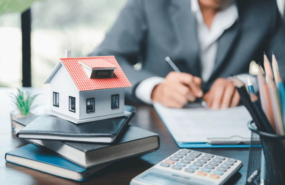 A model home sitting on a stack of notebooks next to a calculator in the office of a mortgage lender.